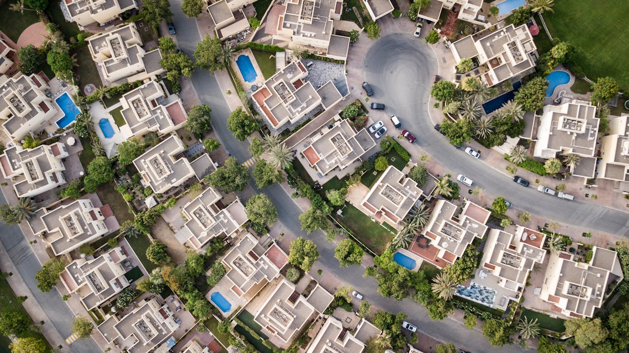 Home Explore a stunning aerial view of a residential area in Dubai with lush greenery and swimming pools.